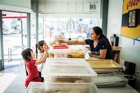 Una trabajadora de la panadería atiende a una clienta y a una niña en el mostrador.