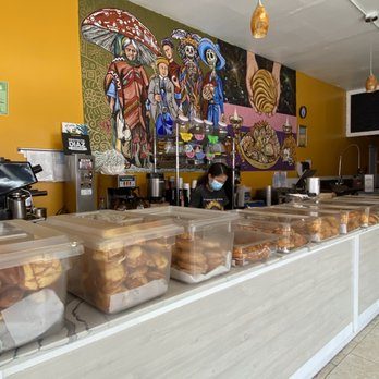 Mostrador de pan dulce con recipientes transparentes frente a un mural colorido.
