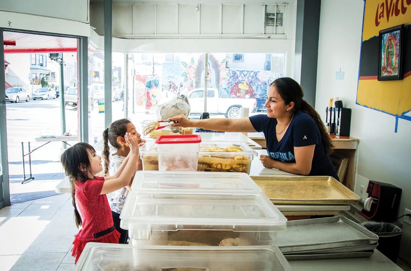 Una trabajadora de la panadería entrega un pan a dos niñas en el mostrador.