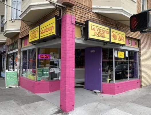 Fachada de esquina de La Victoria, con frente rosa brillante y letreros de La Victoria, Sourdough y Pan Dulce.